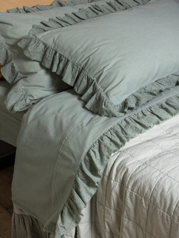 Biancheria da letto con bordi arricciati di colore verde chiaro e copriletto trapuntato bianco.