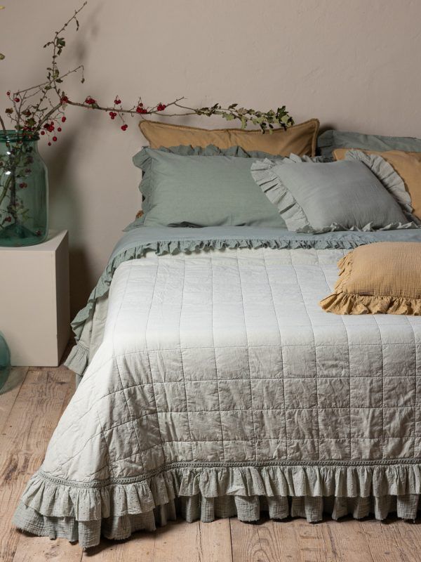 Letto con trapunta verde chiaro e volant, cuscini, tavolino con vaso.