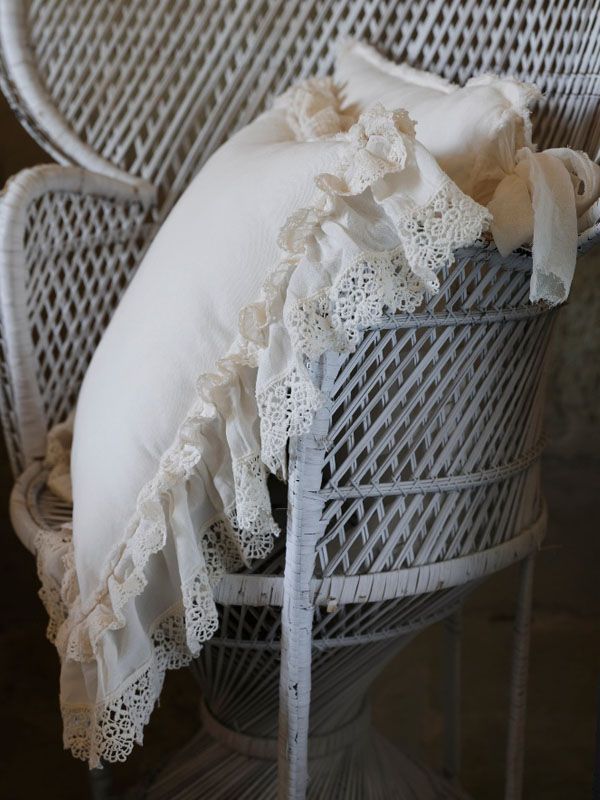 Cuscino bianco con rifiniture in pizzo su una sedia in vimini bianco.