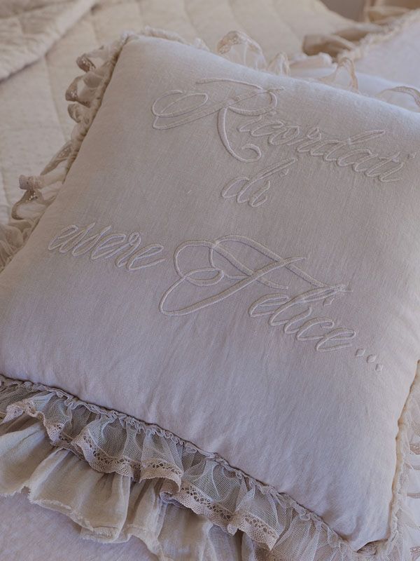 Cuscino color crema con testo ricamato e bordi arricciati, appoggiato su un letto.