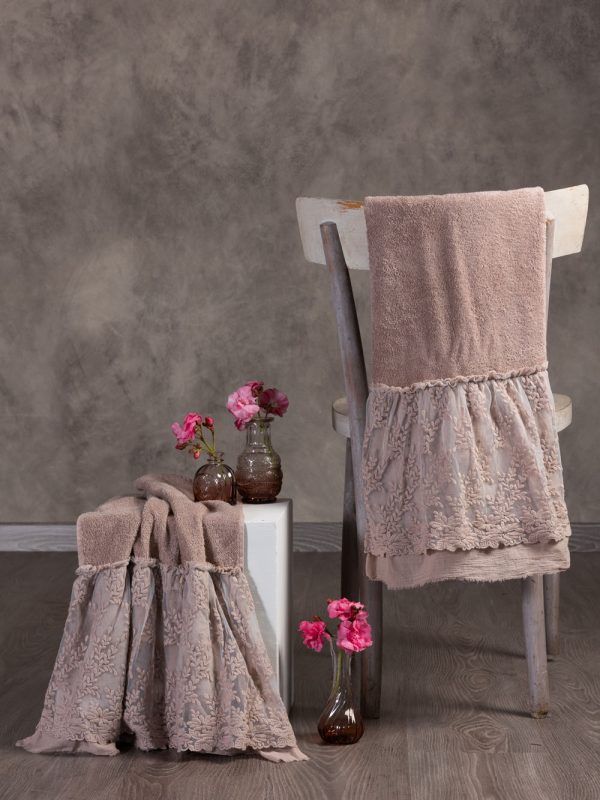 Asciugamani con bordi in pizzo su sedia e cubo, con vasi di fiori rosa. Toni beige.