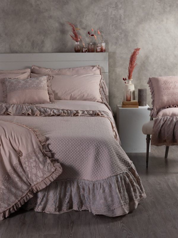 Letto rosa con lenzuola arricciate, cuscini e una sedia coordinata in una stanza dai toni neutri.