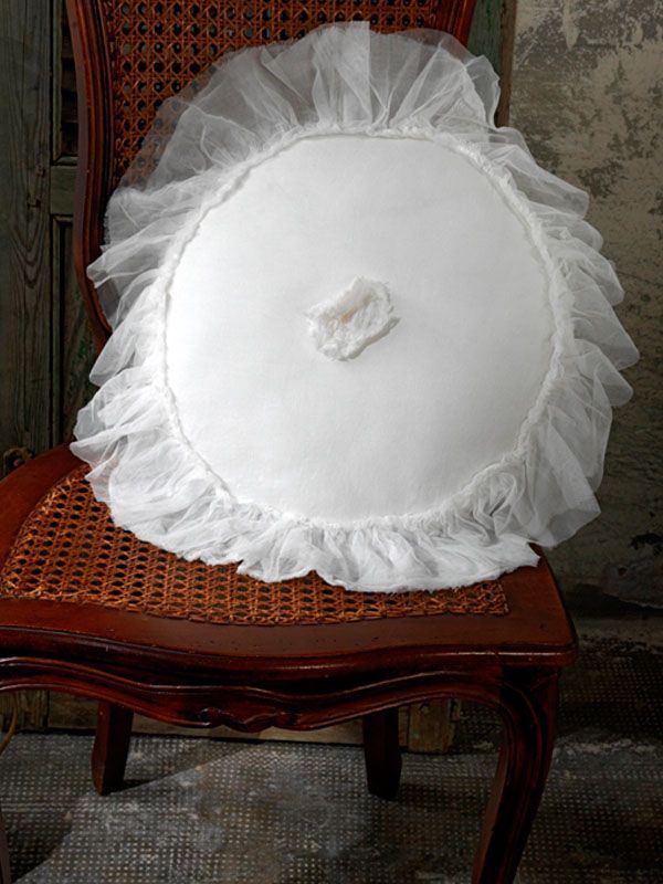 Cuscino bianco con volant su una sedia con schienale in vimini.