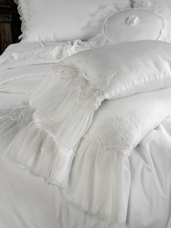Lenzuola bianche con federe arricciate e un cuscino decorativo rotondo.
