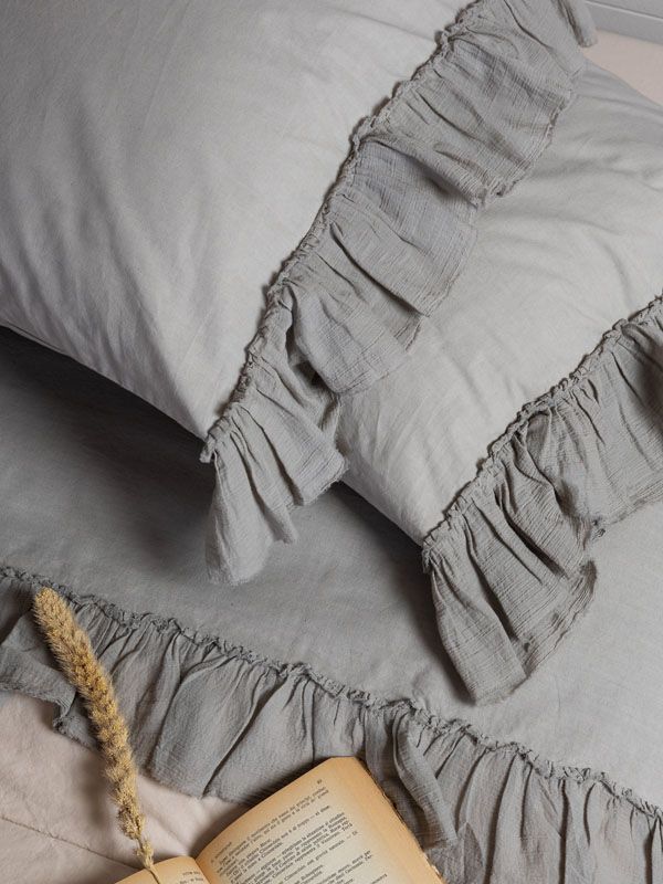 Lenzuola grigie arricciate con un cuscino e un libro aperto.