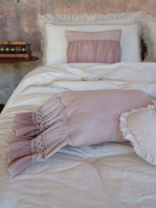 Letto con lenzuola bianche e cuscini decorativi rosa con volant, in una stanza dai toni tenui.