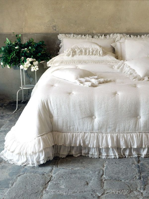 Biancheria da letto bianca con bordi arricciati su un letto in una stanza rustica.
