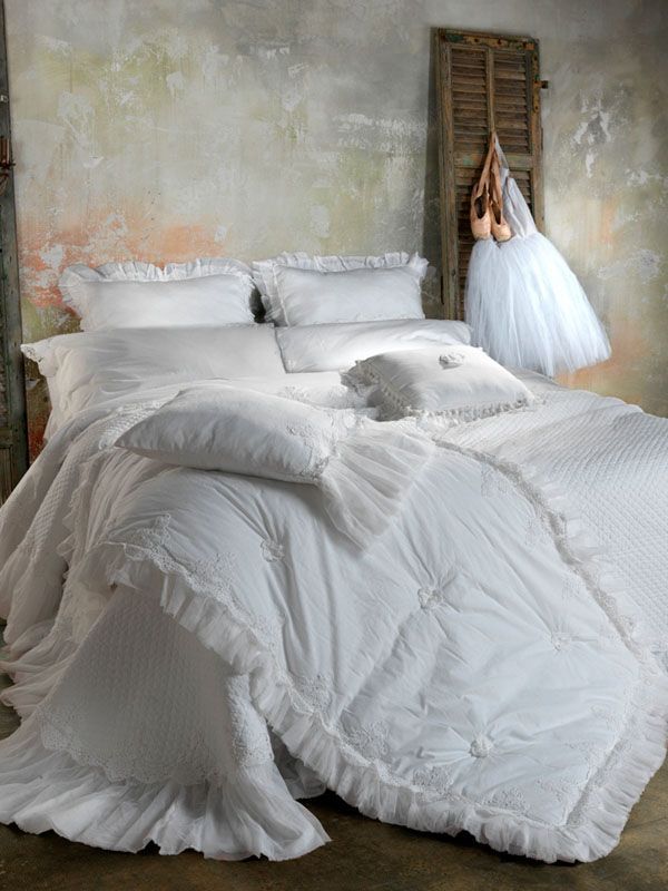 Lenzuola bianche con volant sul letto, con cuscini. Un tutù da balletto e delle scarpette sono appesi alla parete.