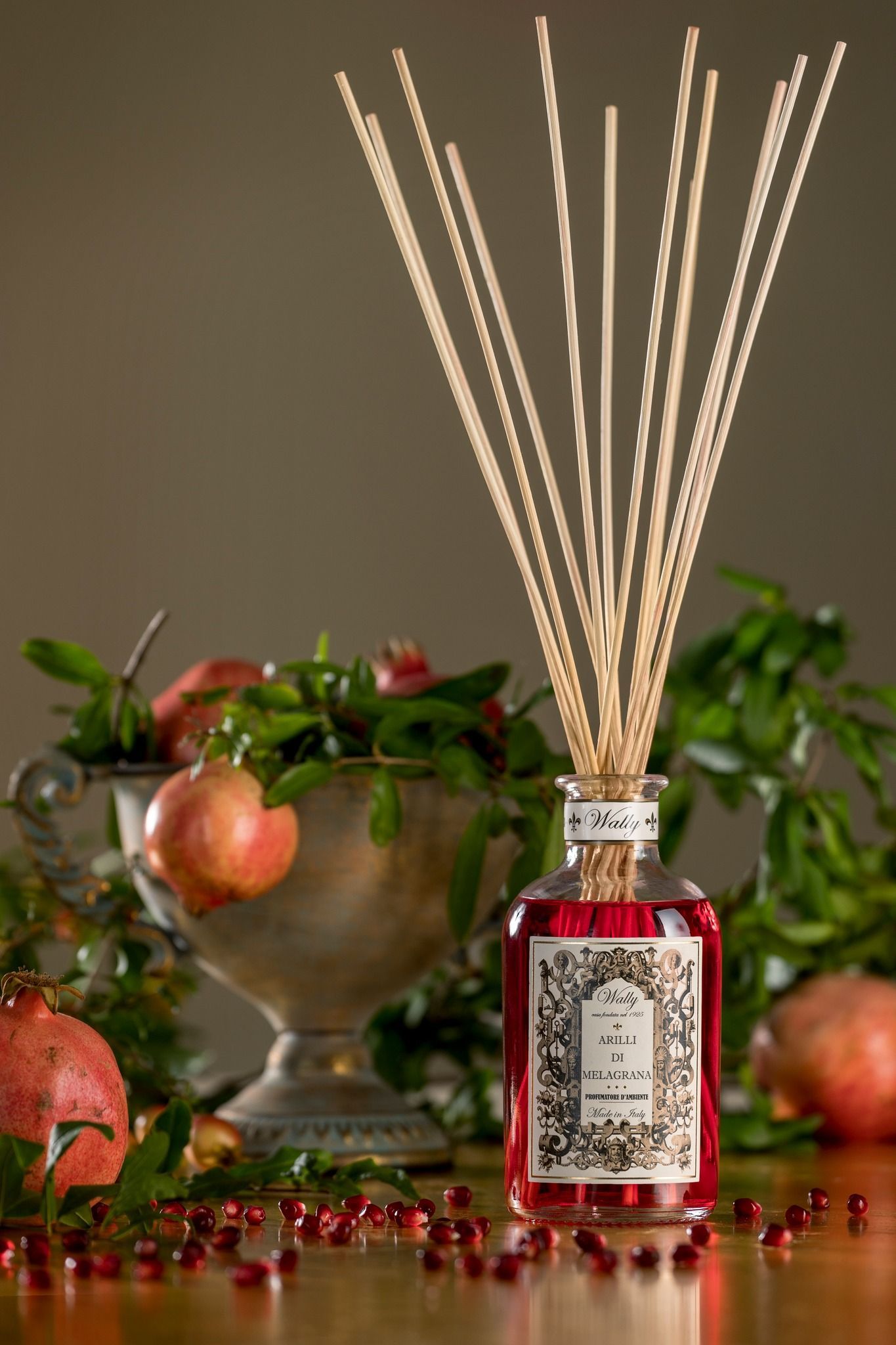 Diffusore a bastoncini con liquido rosso, bastoncini e una natura morta di melograno.