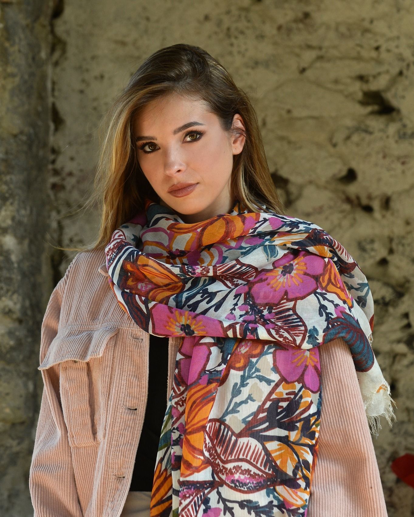 Donna che indossa una sciarpa floreale e una giacca rosa e guarda l'osservatore.