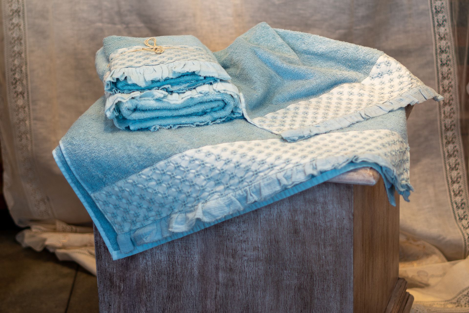 Asciugamani blu con bordi in pizzo bianco, impilati su un blocco di legno, su uno sfondo beige.