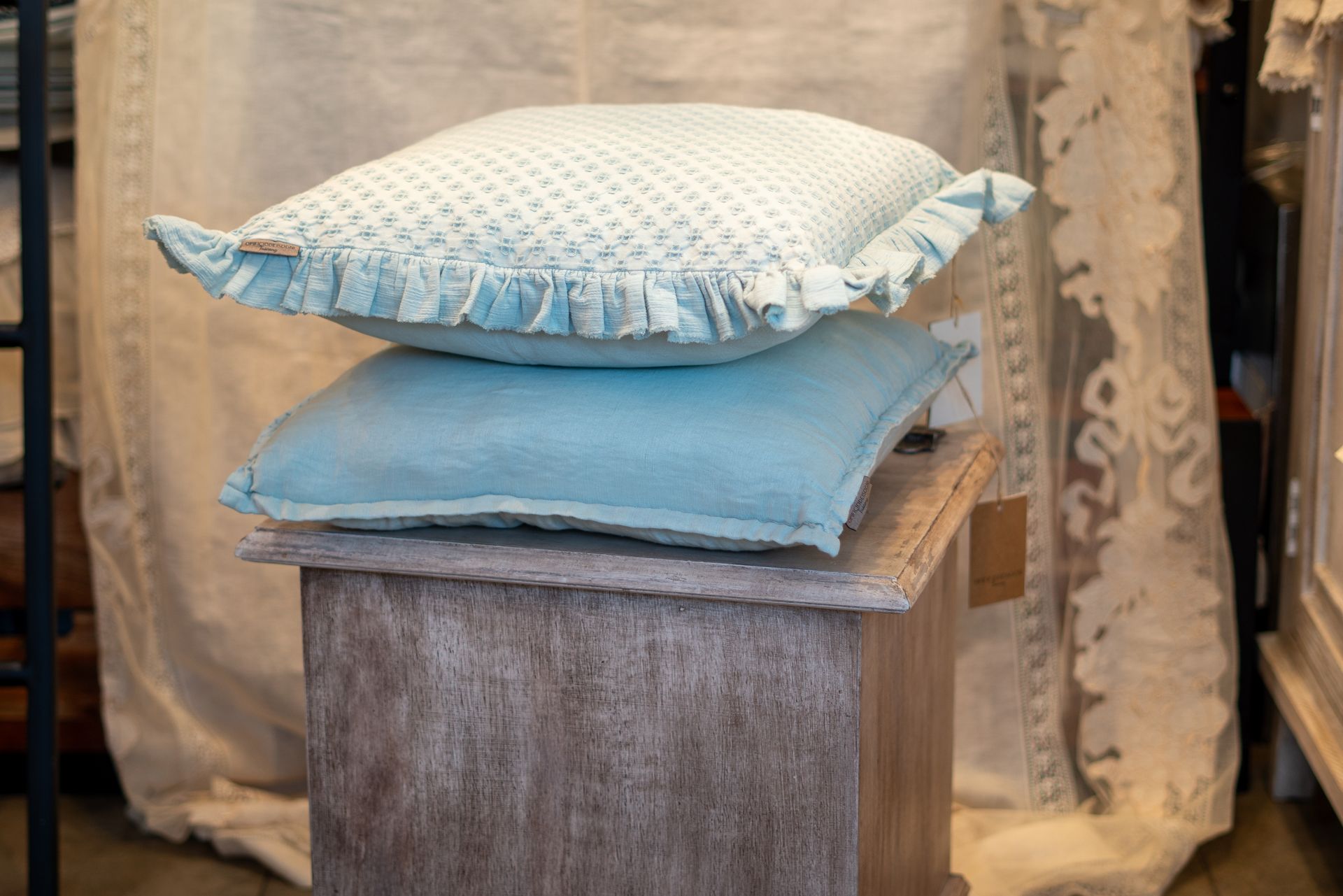 Due cuscini blu impilati su un tavolino di legno, con una tenda a fantasia sullo sfondo.