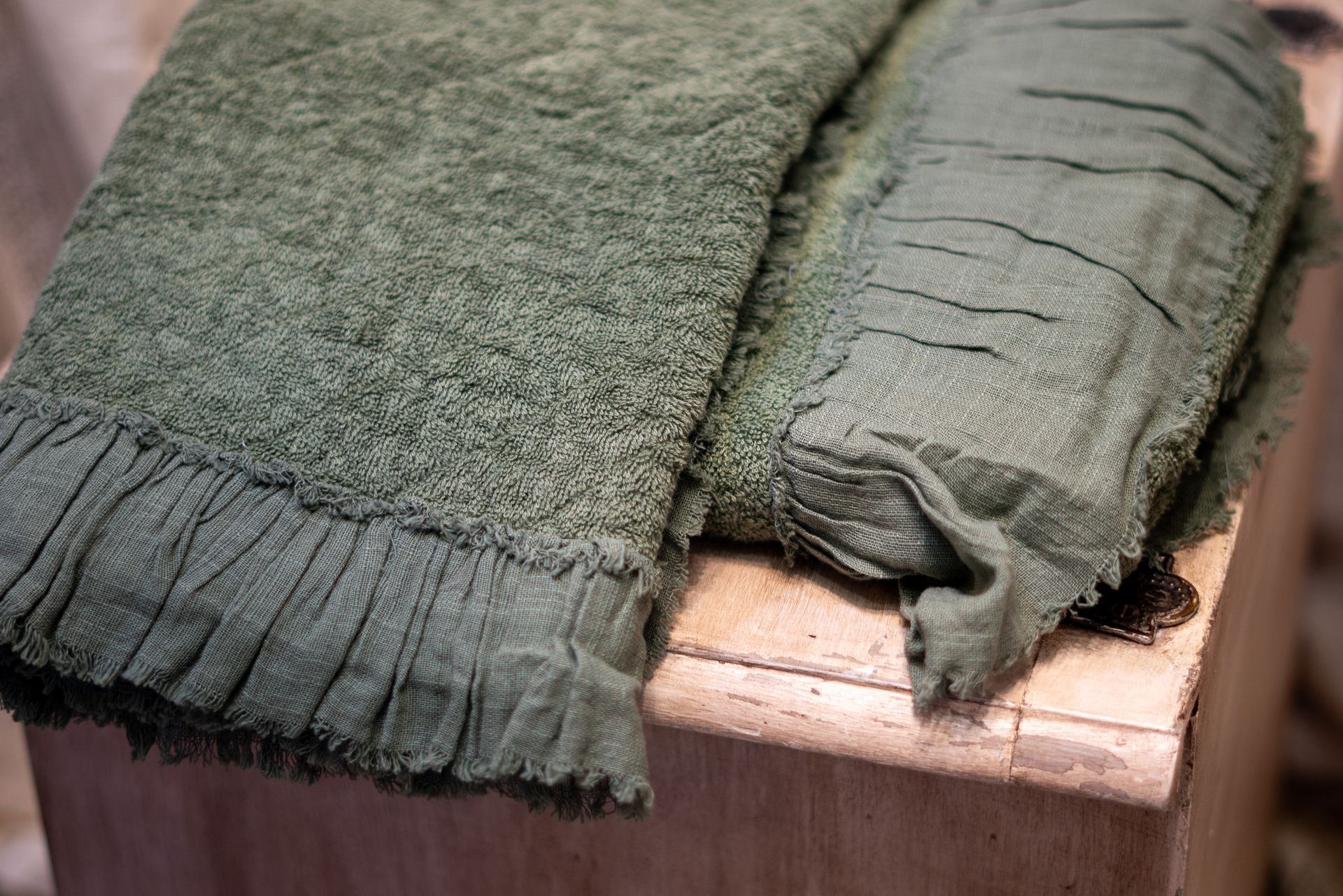 Due asciugamani verde oliva con frange testurizzate, piegati su una superficie di legno.