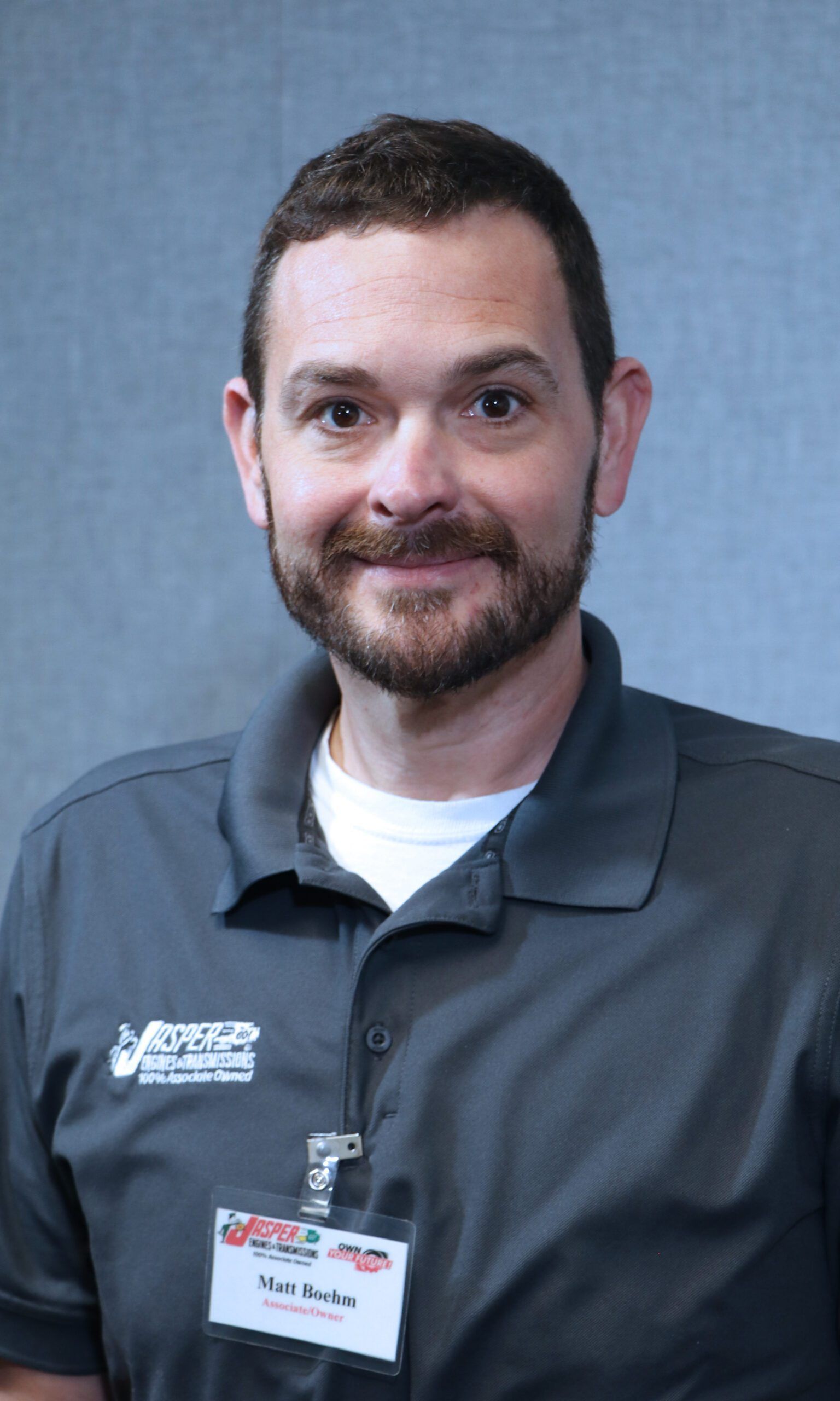 Man wearing gray polo shirt, name tag, smiling.
