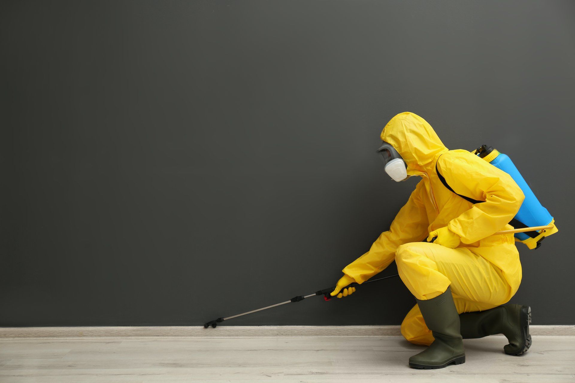 Un homme en combinaison de protection jaune pulvérise un mur avec un pulvérisateur.