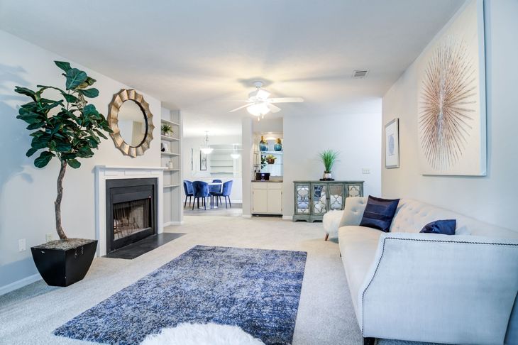 Living room with fireplace, couch, and large blue rug. A dining area is visible in the background.