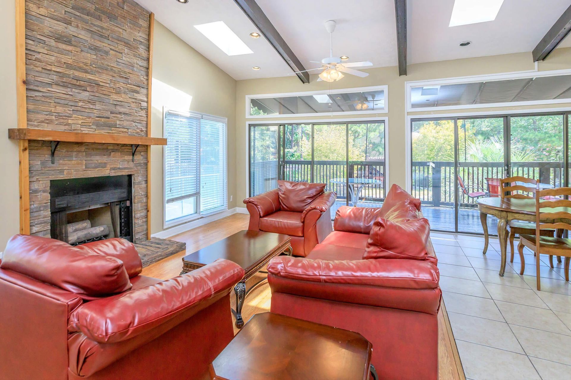 Red leather furniture, stone fireplace, and large windows overlooking a deck.