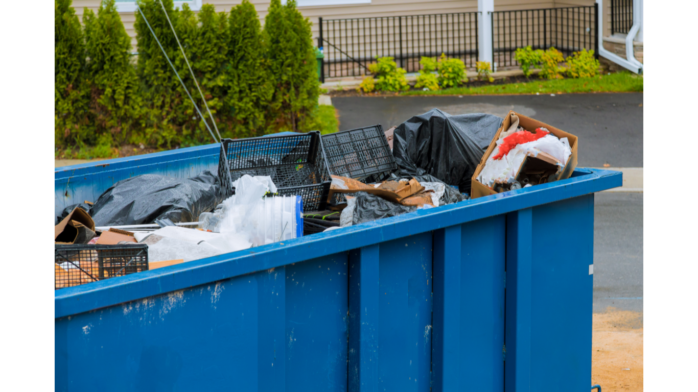 Blue dumpster overflowing with trash outside a house.