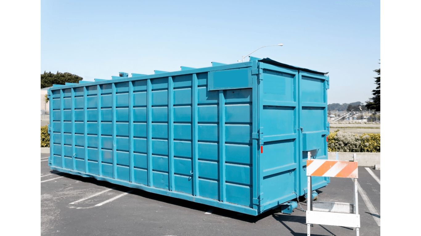Blue dumpster in a parking lot under a clear sky, with an orange and white barricade.