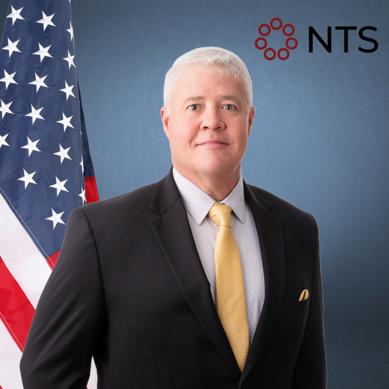 A man in a suit and tie stands in front of an american flag