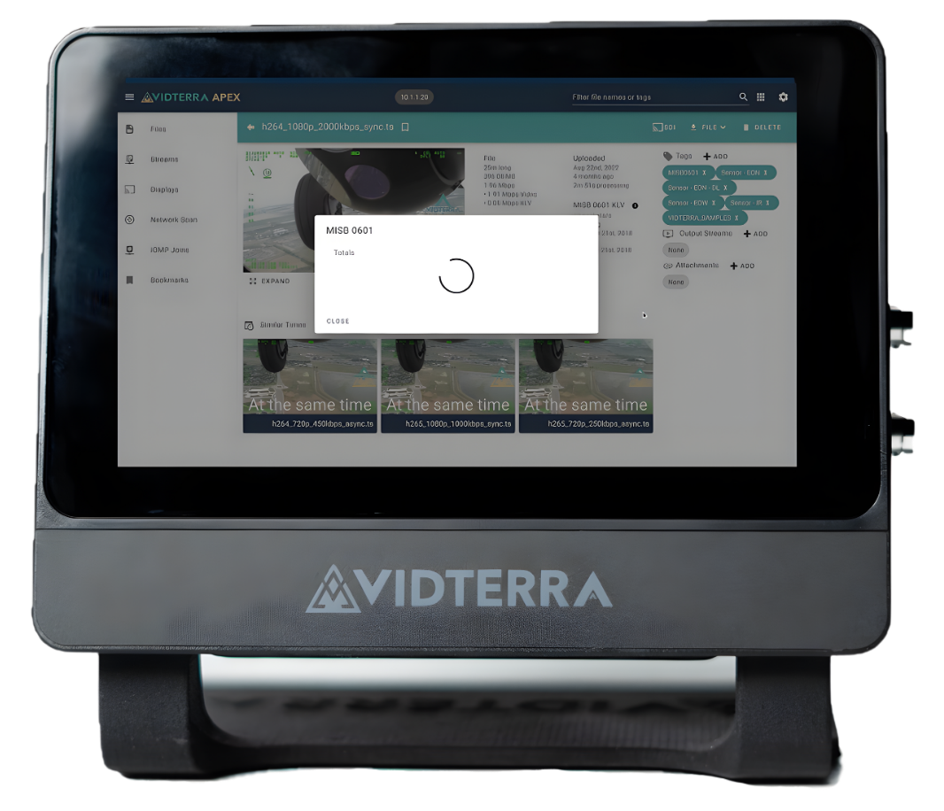 A tablet-like device displays a video interface with a loading symbol on screen. The device is labeled 