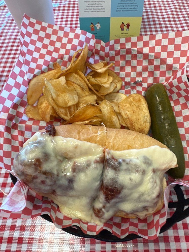 A sub sandwich with chips and a pickle on a checkered table cloth
