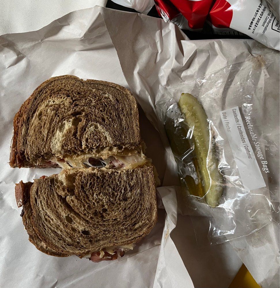 A sandwich and a pickle are wrapped in plastic
