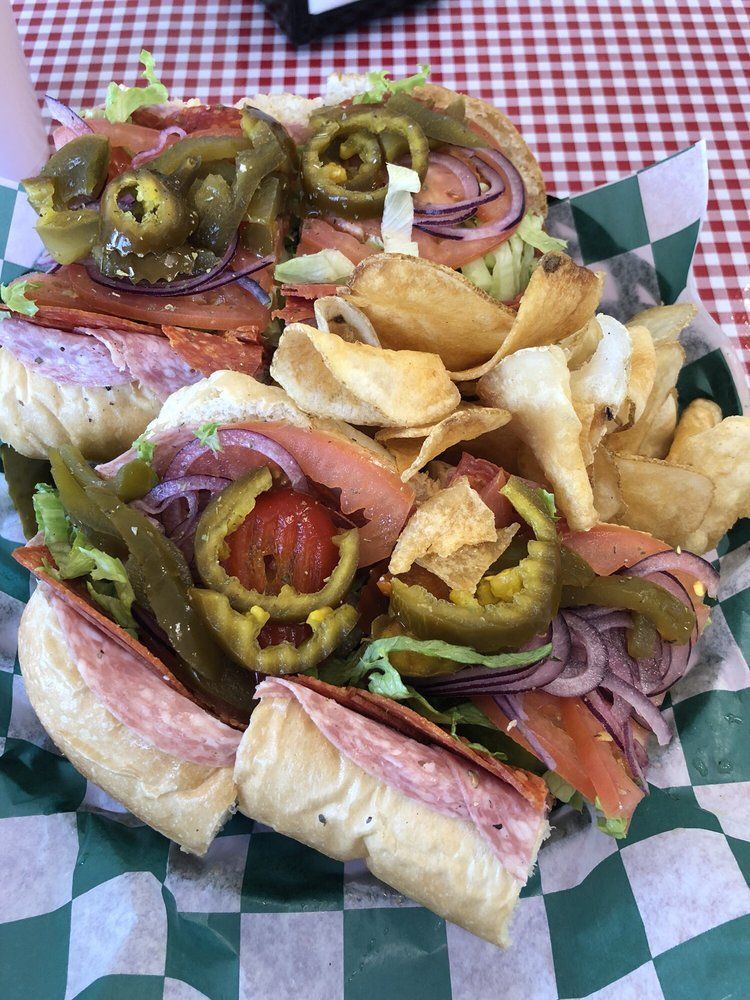 A sub sandwich with potato chips on a checkered paper on a table