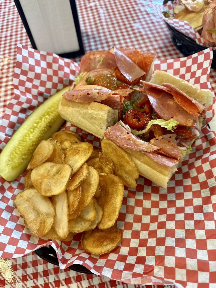 A sandwich with french fries and a pickle on a checkered table cloth