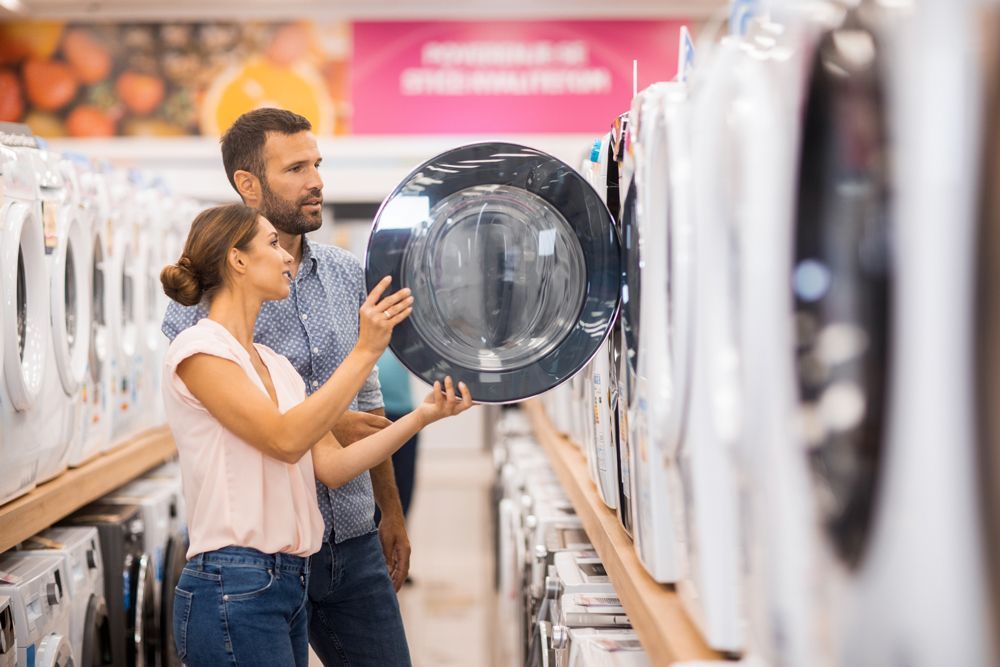 A man and a woman are looking at a washing machine in a store.