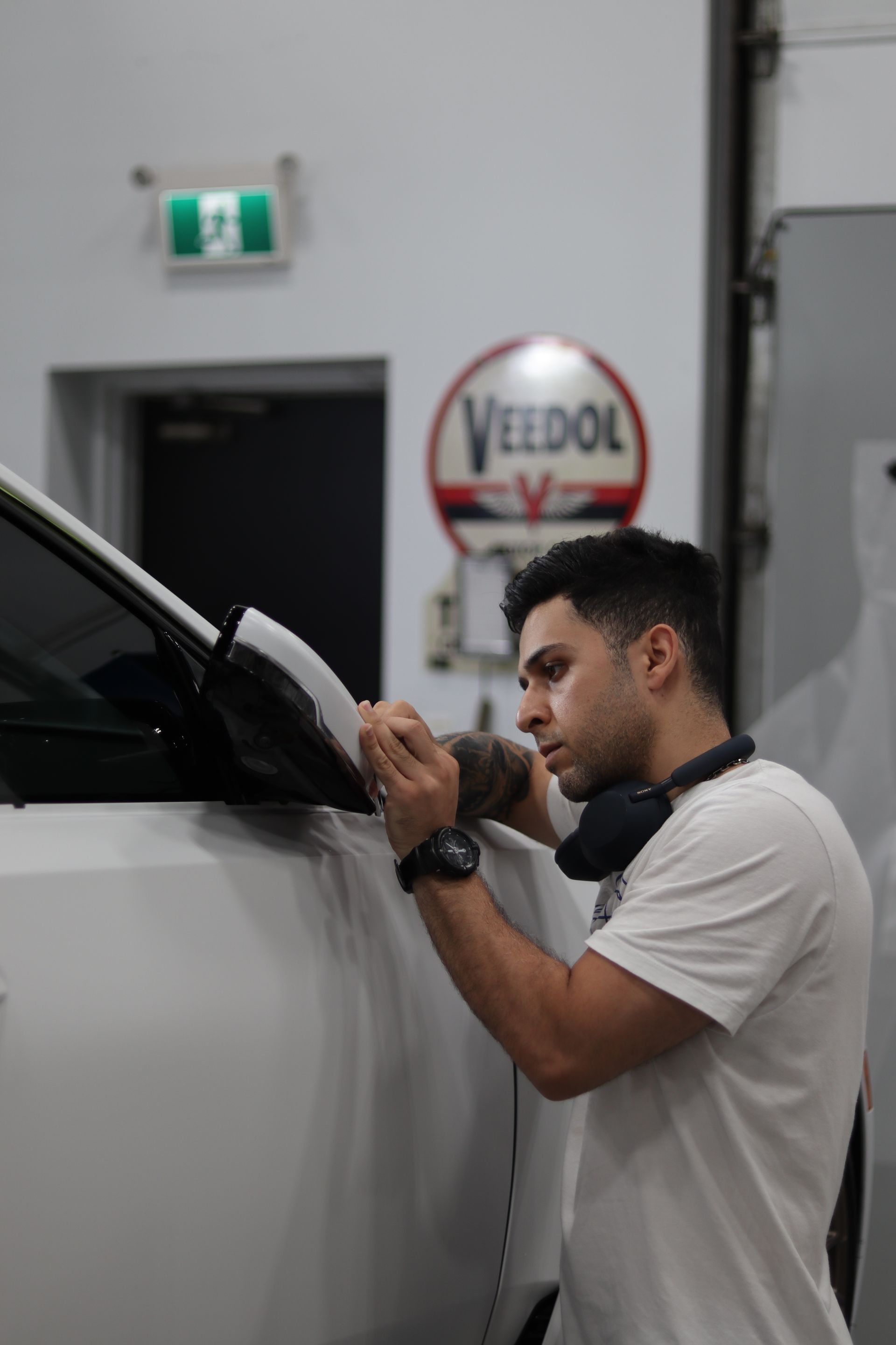 Man polishing a white car in a garage, working near the side mirror.