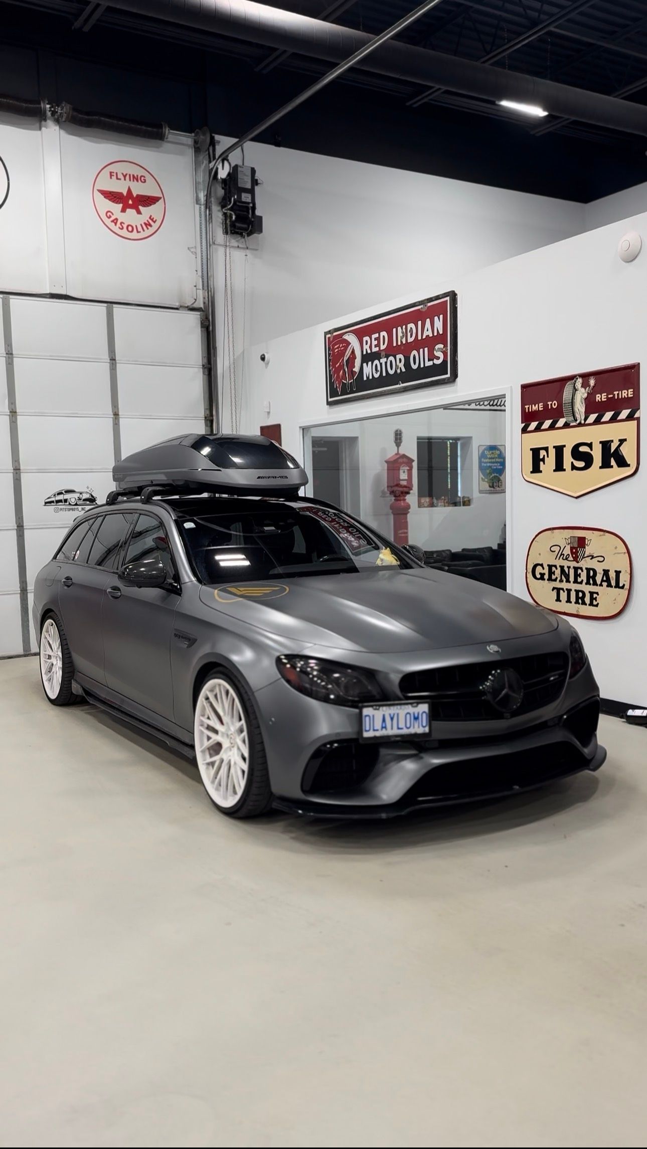Gray sports sedan in an auto shop garage with a roof cargo box and racing decals