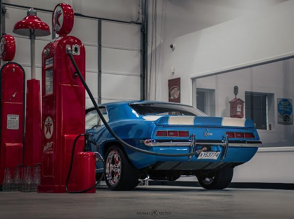 Blue classic muscle car in a garage beside a red vintage gas pump and garage equipment