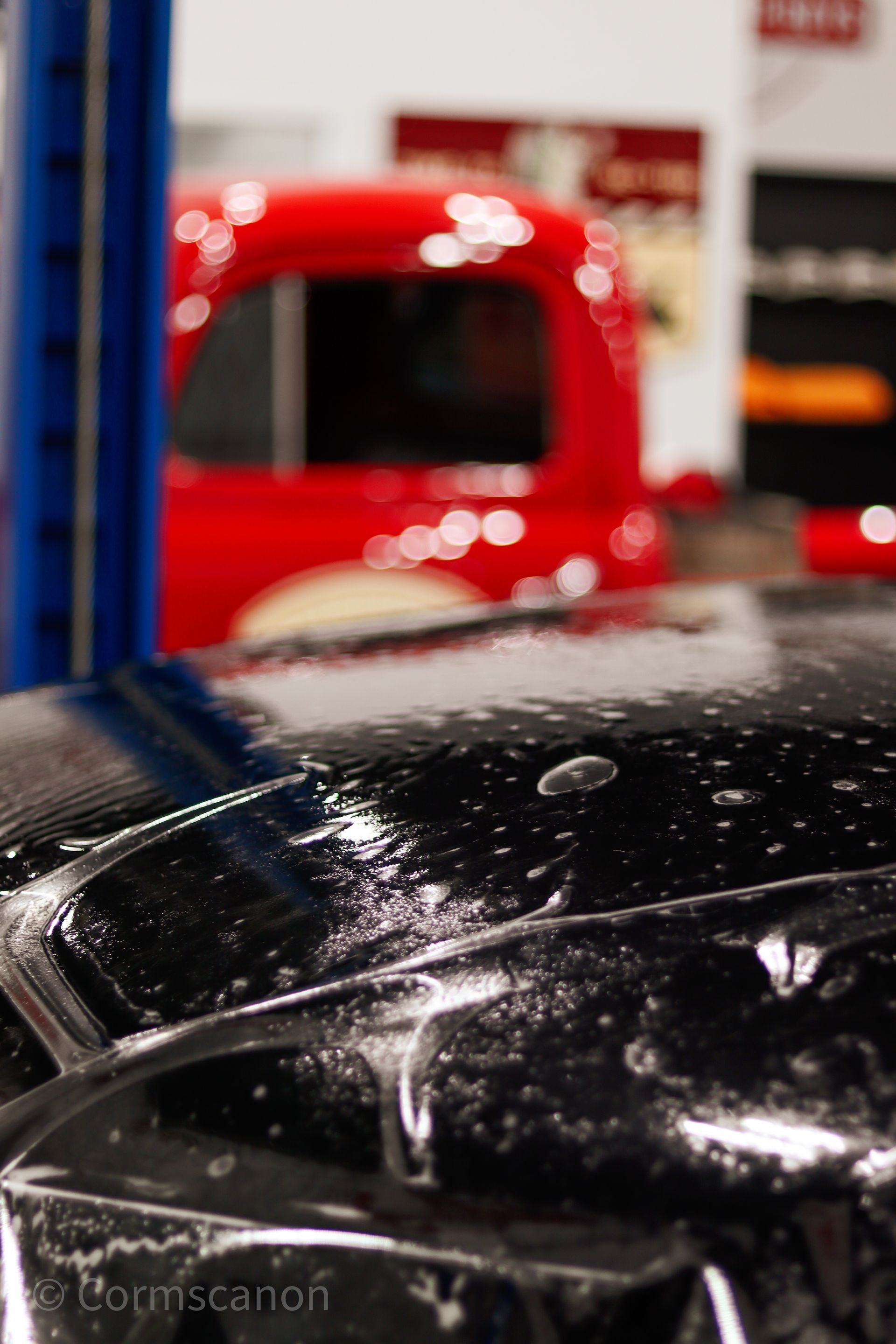 Man in a workshop behind a car lift, with a blurred car in the foreground and a tripod in the background
