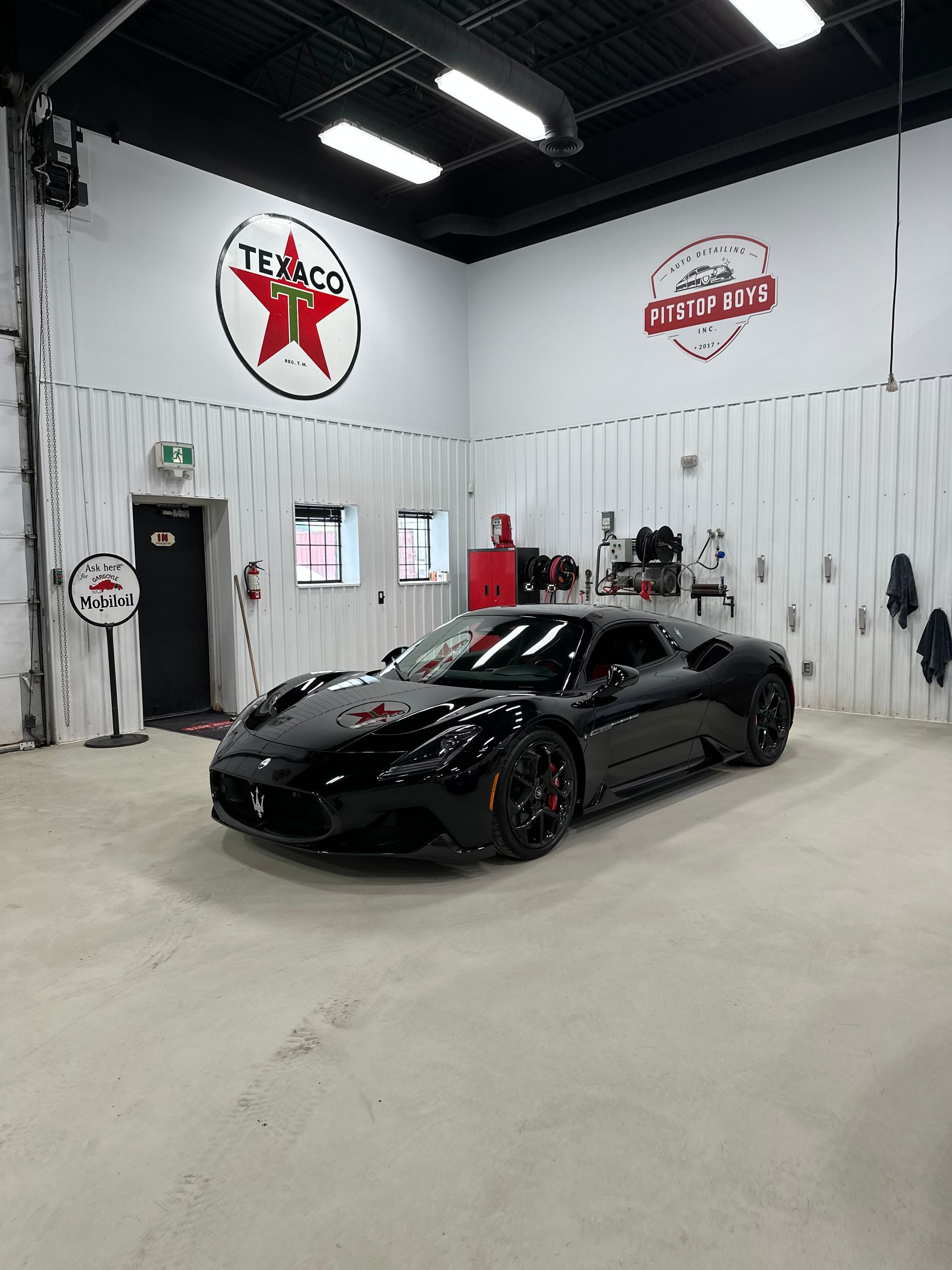 Black sports car in a clean auto shop with white walls and Shell logos