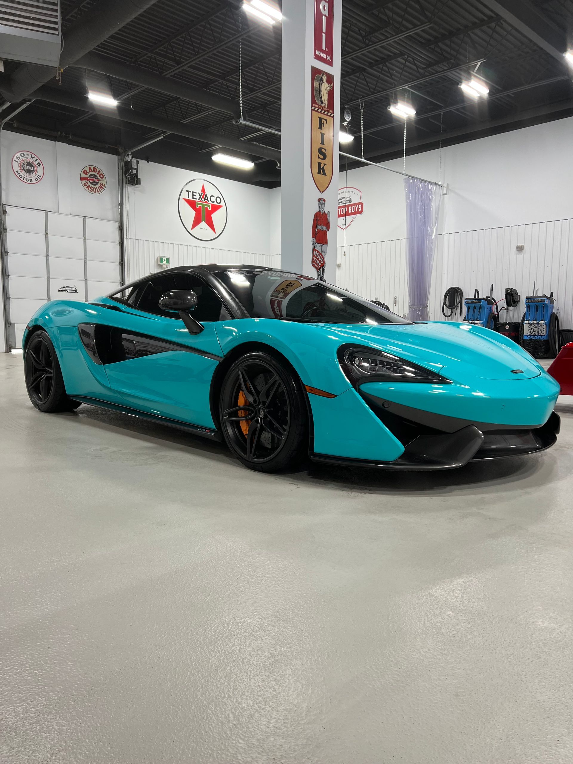 Turquoise sports car with black accents displayed indoors at an auto show