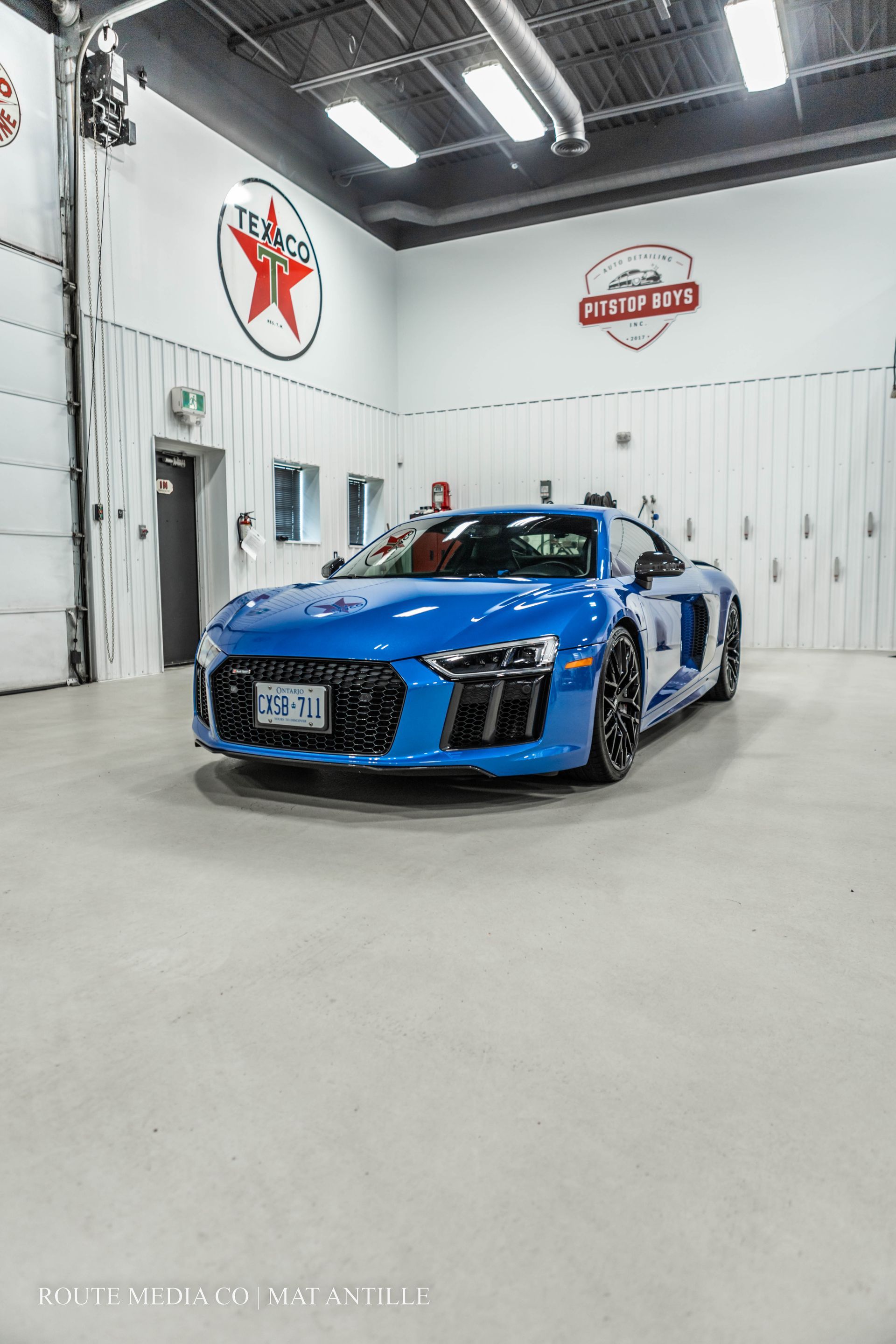 Blue sports car parked outside a garage with Red Indian Motor Oils signage