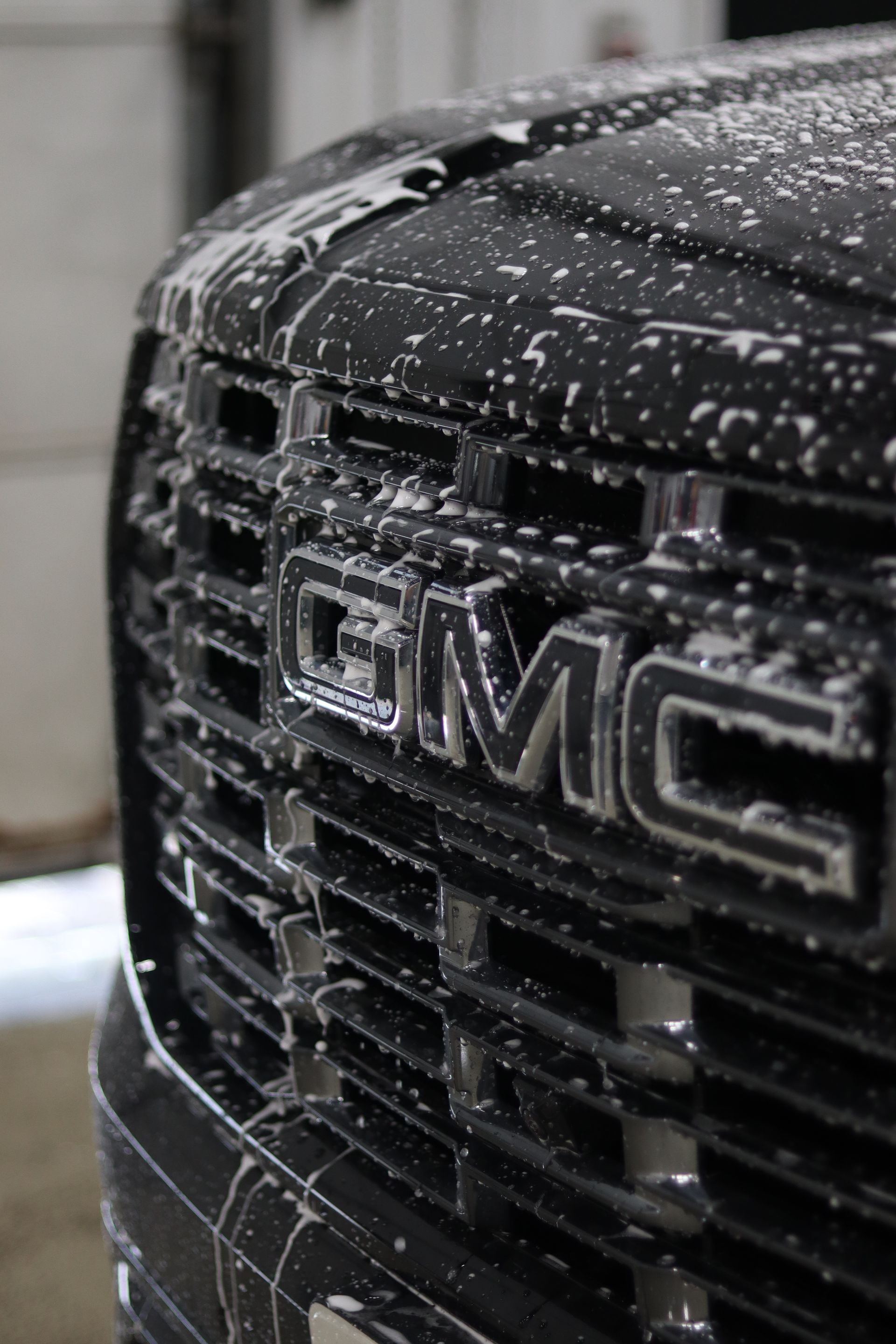 Close-up of a GMC truck grille covered in soap suds and water droplets.
