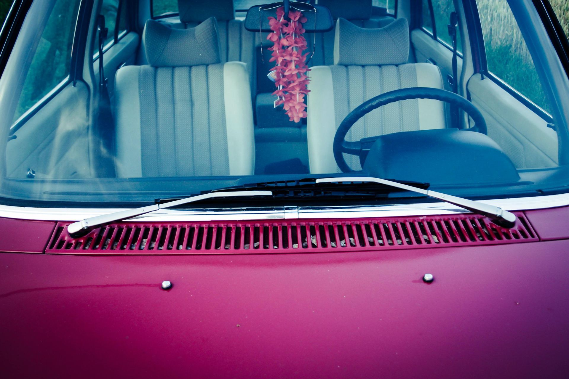 Pink car dashboard and windshield with hanging flower garland and a blue steering wheel
