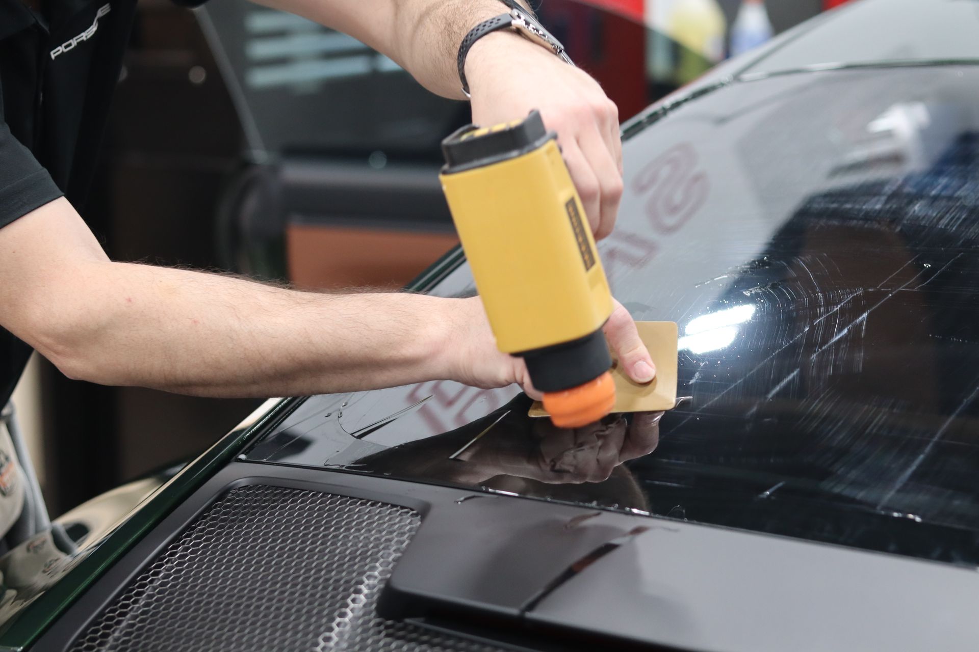 Person using a yellow tool to apply adhesive or sealant on a car windshield