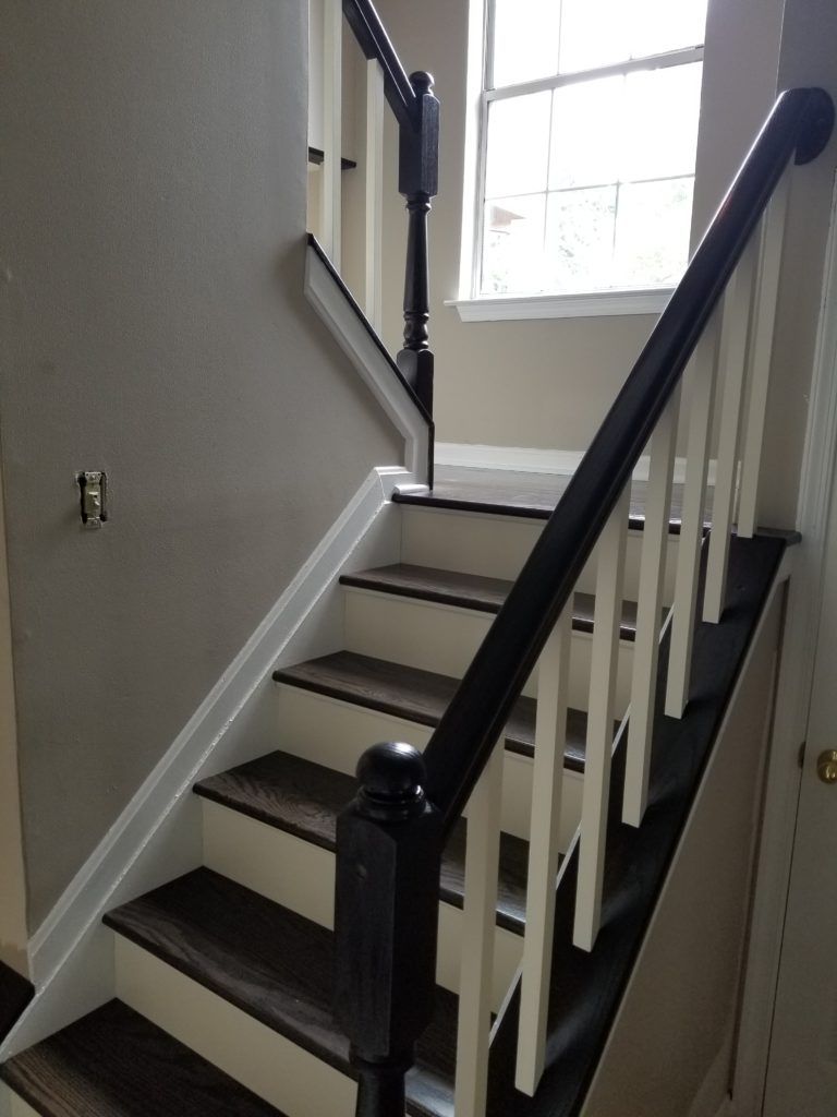 Staircase with dark treads, white risers, and a black handrail next to white balusters. A window is at the top.