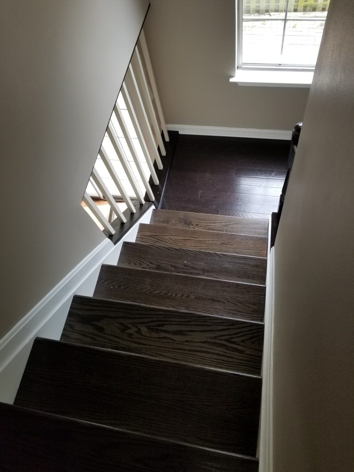 Dark wooden staircase leading up to a window, white trim and railing, neutral-toned walls.