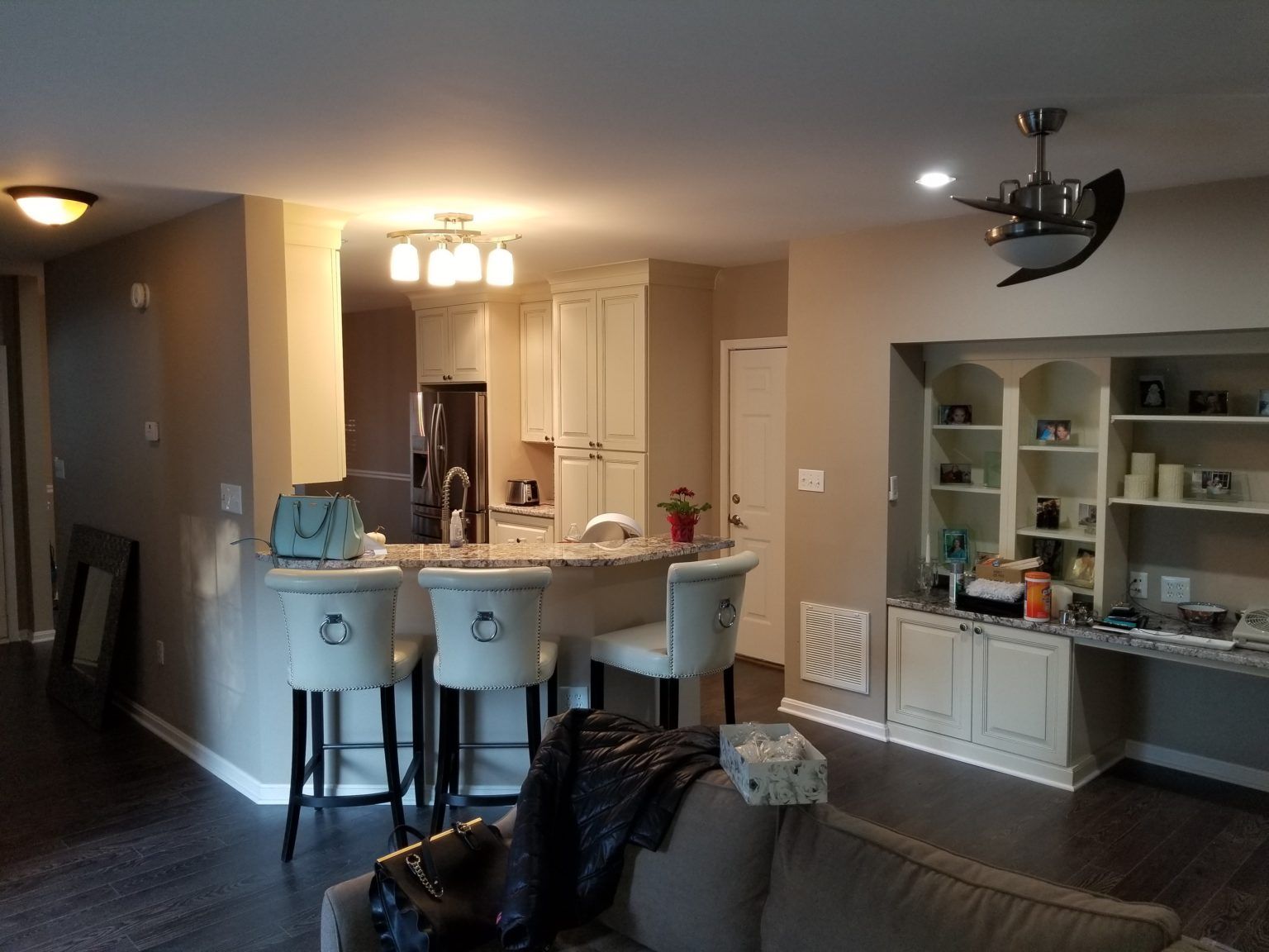 Interior view of a kitchen with a bar, white cabinets, and living area with built-in shelves and a ceiling fan.
