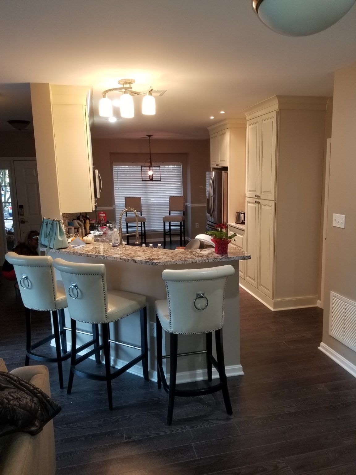 Kitchen with a bar, stools, and cabinetry; dark wood flooring and tan walls.