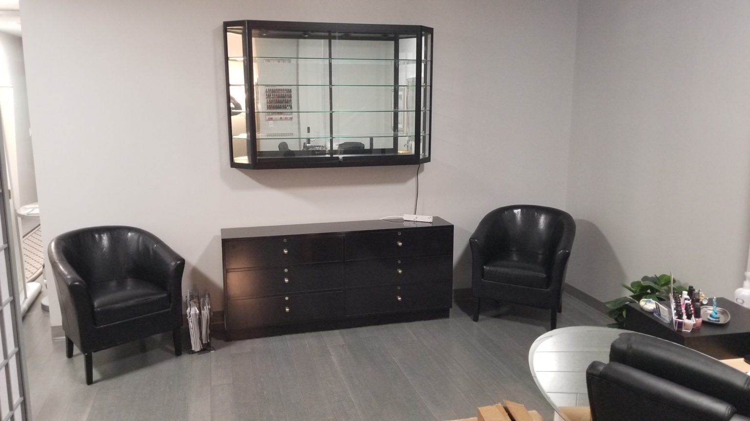 Awaiting area with black chairs, cabinet, and display case on a gray wall.