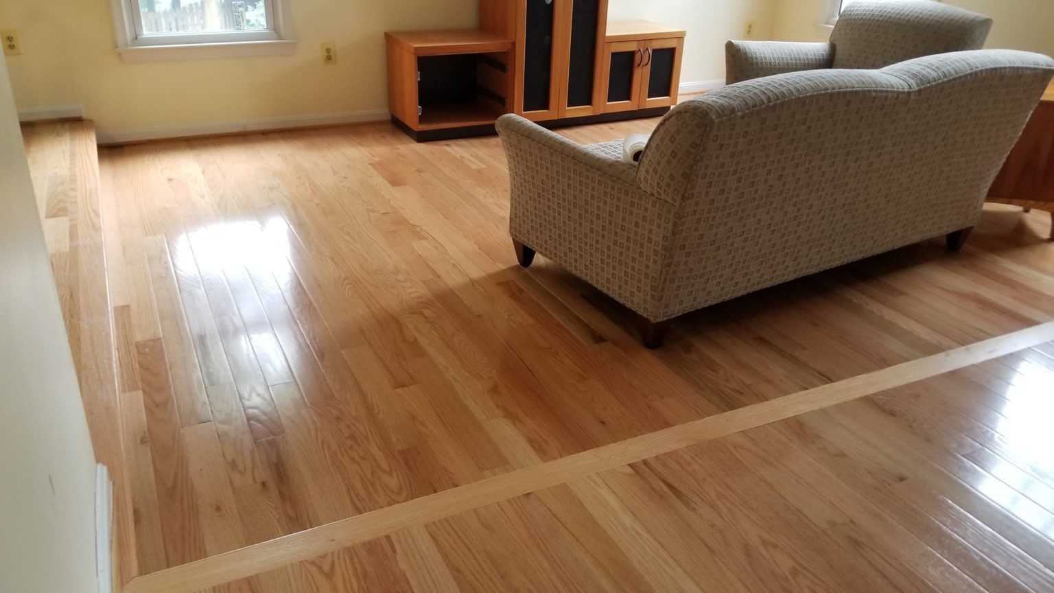 Wooden floor with a step down, leading to a living room with a couch and entertainment center.