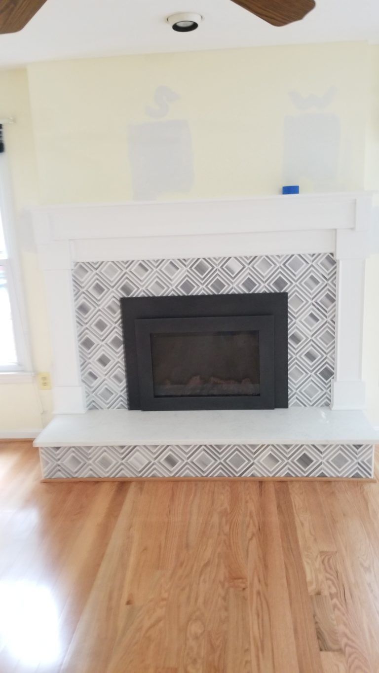 Fireplace with black insert, gray and white patterned tile, white mantel, light wood floors, and yellow walls.