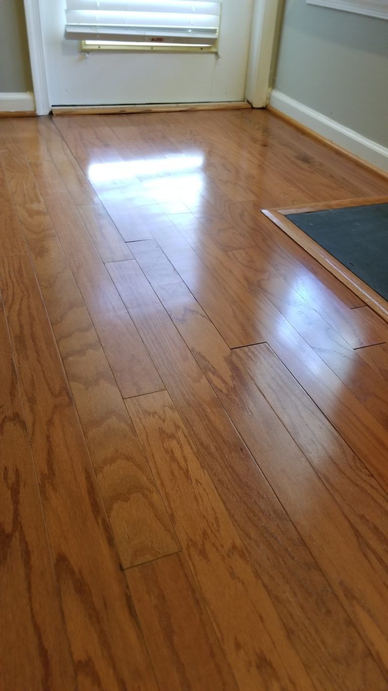 Wooden floor with damage, near a door and a dark mat.