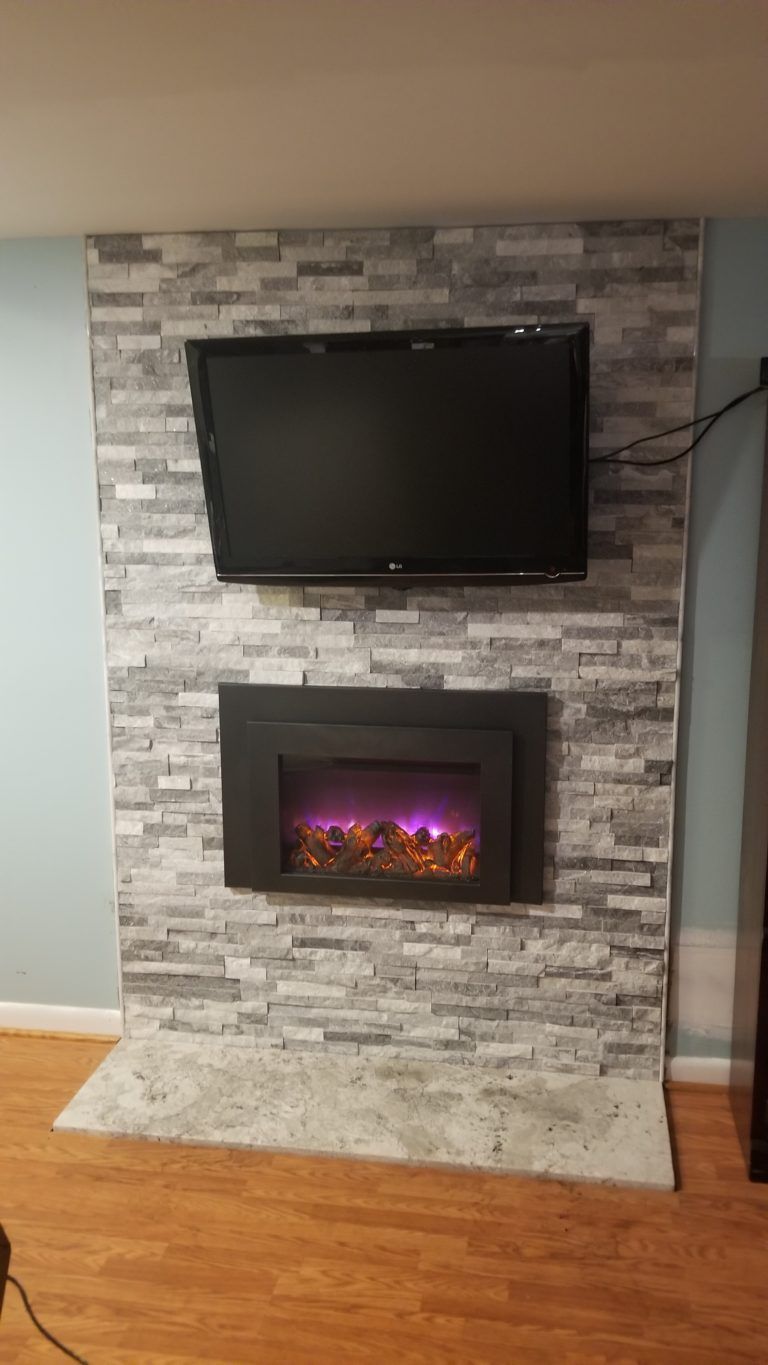 Electric fireplace and TV mounted on a gray brick-patterned wall. A white rug is on the floor.