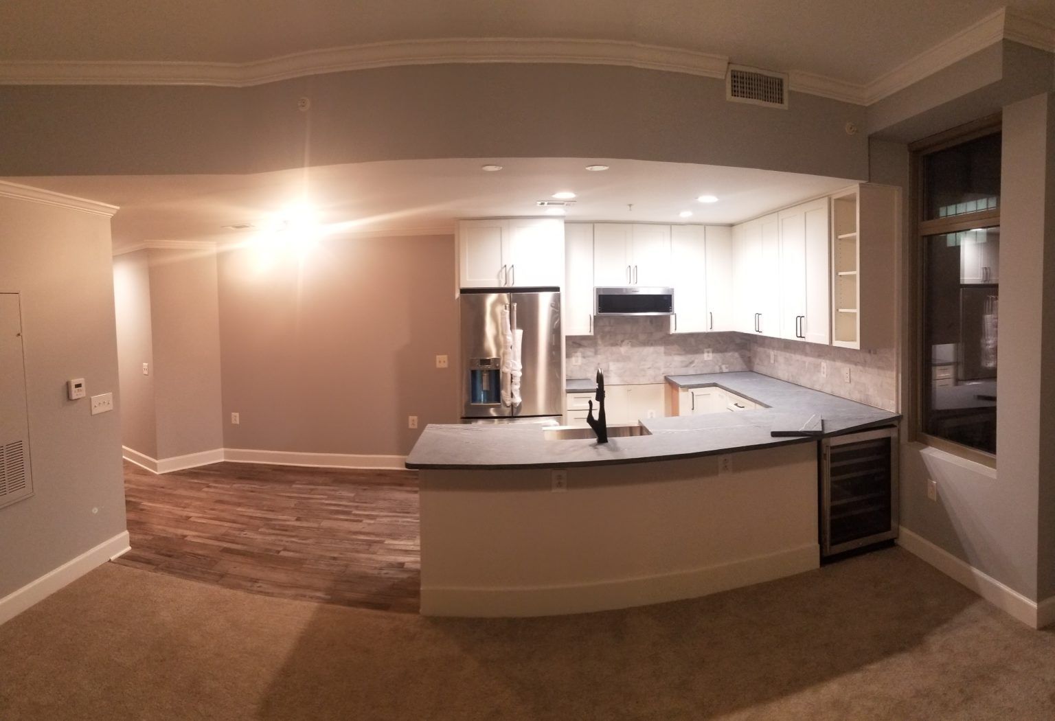 Modern kitchen with light gray walls, white cabinets, and dark countertop, with a wine fridge.